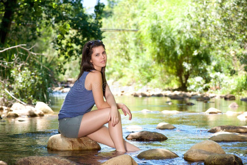 Woman sitting on rock by a stream with bare feet in water