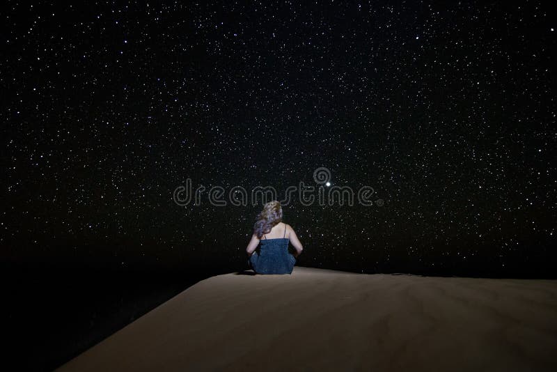 A woman sitting staring at the starry sky towards Venus, on a dune in the Erg Chebbi desert