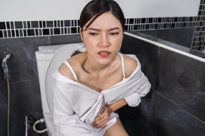 Woman sitting on toilet in the bathroom and holding her painful Stomach.