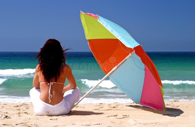I giovani, in forma, sani donna seduta sotto colorato ombrellone sulla spiaggia di sabbia bianca di fronte al mare in una giornata di sole in vacanza.
