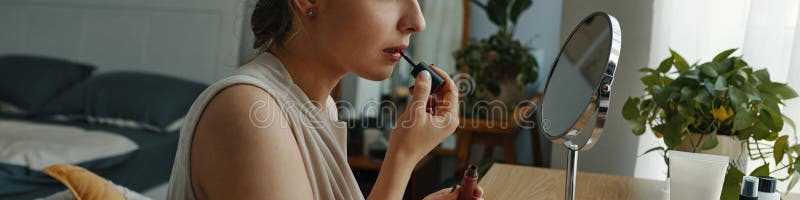 Woman Applying Lipstick in Modern Bedroom Setting stock photo
