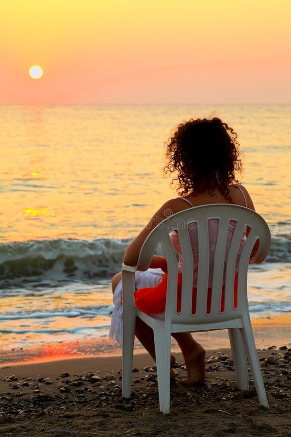 Woman sitting on white plastic chair on beach