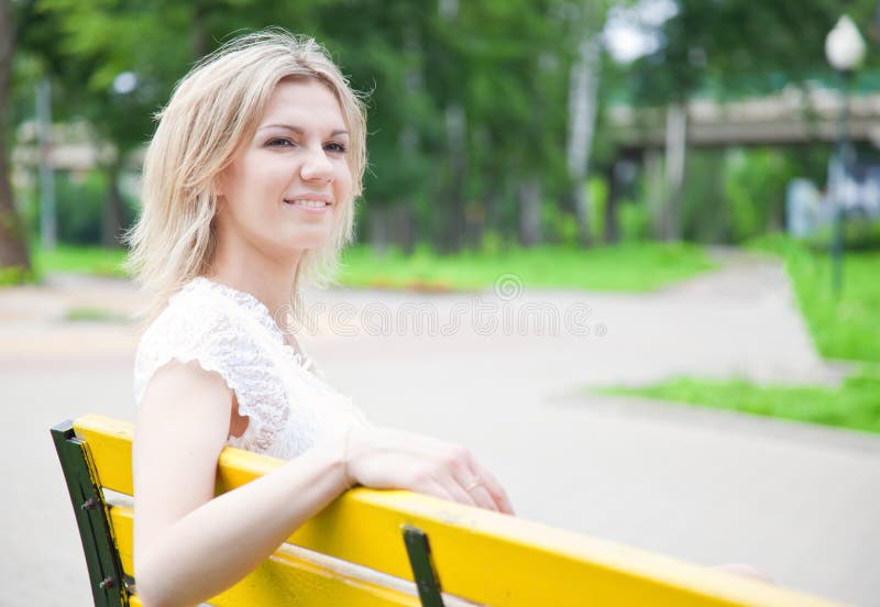 Woman is sitting on the yellow bench in the park