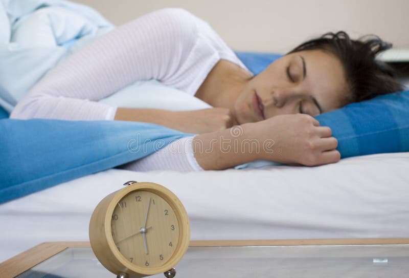 Brunette woman sleeping in bed with alarm clock in the foreground. Brunette woman sleeping in bed with alarm clock in the foreground