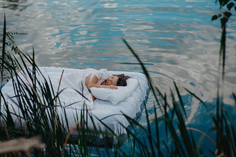 Woman sleeps on a mattress floating in the water among plants