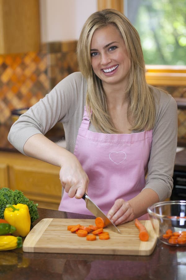 A young woman is slicing carrots in her kitchen and smiling at the camera. Vertically framed shot. Top smiling cheerful stock images, royalty-free photos and pictures