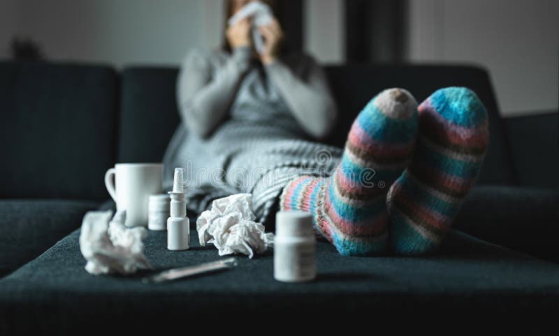 Woman sneezing and blowing nose with tissue and handkerchief. Sick and ill person with flu, cold medicine and woolen socks.