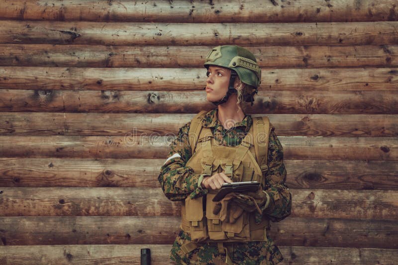 Woman Soldier Using Tablet Computer Against Old Wooden Wall in Camp