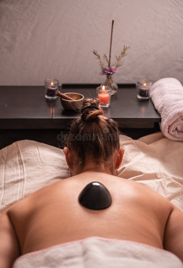 Woman in a spa receiving a relaxation massage with scented candles, incense, scent flowers, and obsidian stones with towels. 2. stock image Woman in a spa receiving a relaxation massage with scented candles, incense, scent flowers, and obsidian stones with towels. 2. stock image