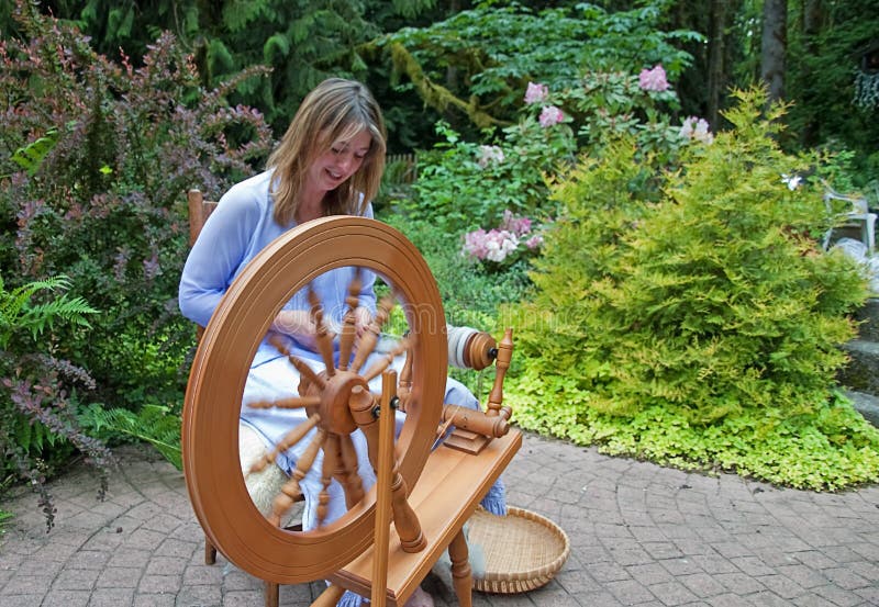 This Woman In Action Is Making Homemade Yarn With A Spinning Wheel From Raw  Wool For A Unique Hand Crafted Work. Shot In A Beautiful Garden Setting.  Stock Photo, Picture and Royalty