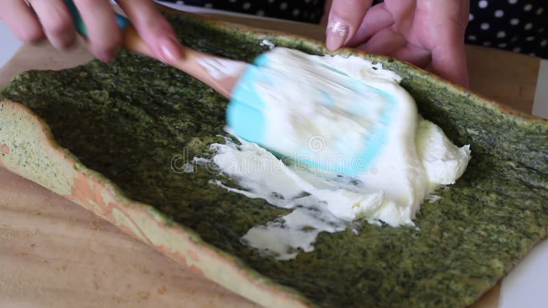 A woman spreads cream with biscuit cake with the addition of spinach and mint. The process of making Swiss roll stock footage