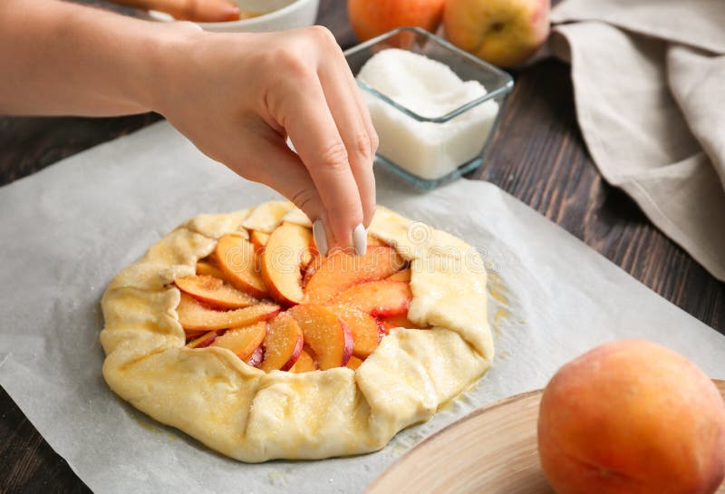 Woman sprinkling raw peach galette with sugar, closeup stock photography Woman sprinkling raw peach galette with sugar, closeup stock photography