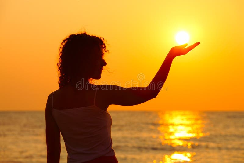 Woman standing on beach, holding sun in hand