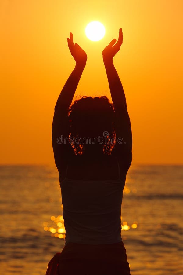 Hermoso mujer joven de pie sobre el Playa, seguimiento atardecer, posesión el sol en manos.