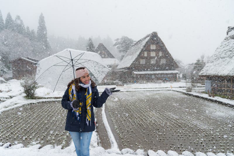 Woman standing and holding transparent umbrella in the winter and snow is falling. With background of ancient house