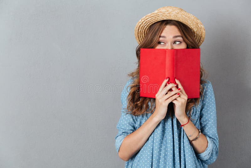 Woman standing over grey wall wearing hat covering face