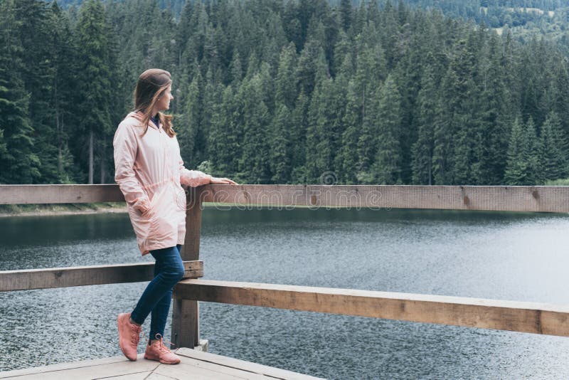 Woman standing in pier near mountain lake and forest