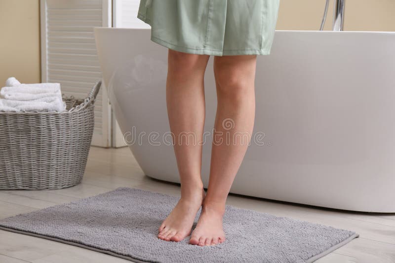 Woman standing on soft grey bath mat near tub at home, closeup