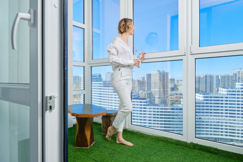 Woman stands on the balcony of her new apartment and admires the view of the city from the window