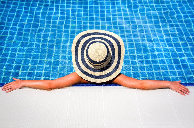 Una mujer en paja un sombrero relajante nadar piscina.