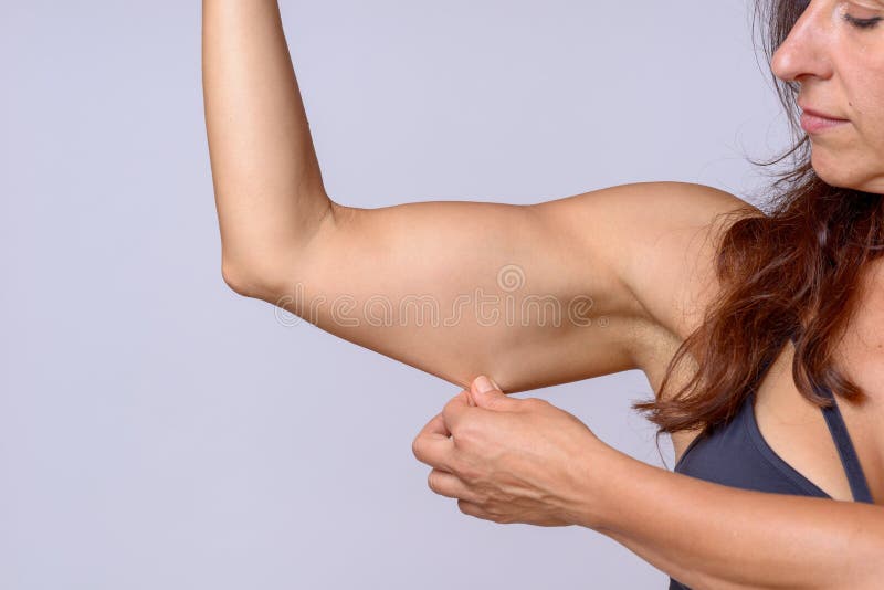 Adult woman with brown hair stretching under arm skin as she flexes muscle over plain white background. Adult woman with brown hair stretching under arm skin as she flexes muscle over plain white background