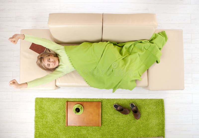 Smiling woman in blanket stretching on living room couch after nap, coffee on tray. Smiling woman in blanket stretching on living room couch after nap, coffee on tray.