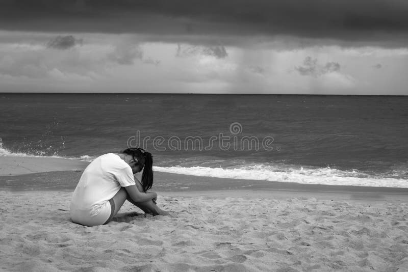 Young sad woman sitting on the beach crying in the rain. Black and white stock images Young sad woman sitting on the beach crying in the rain. Black and white stock images