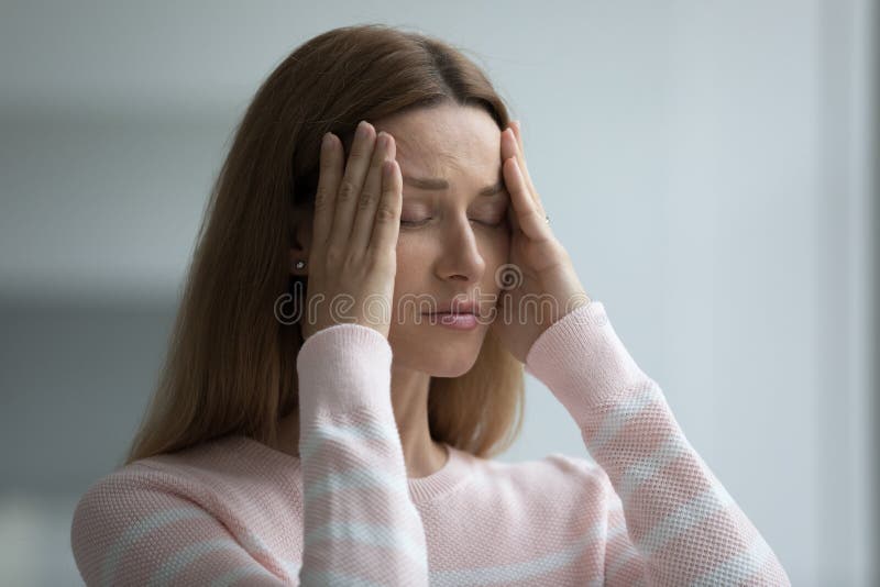 Young woman suffers from intense headache, touch temples try relieving painful feelings with eyes closed, feels badly due to stressful situation, hurt, emotional concerns, physical malaise or migraine