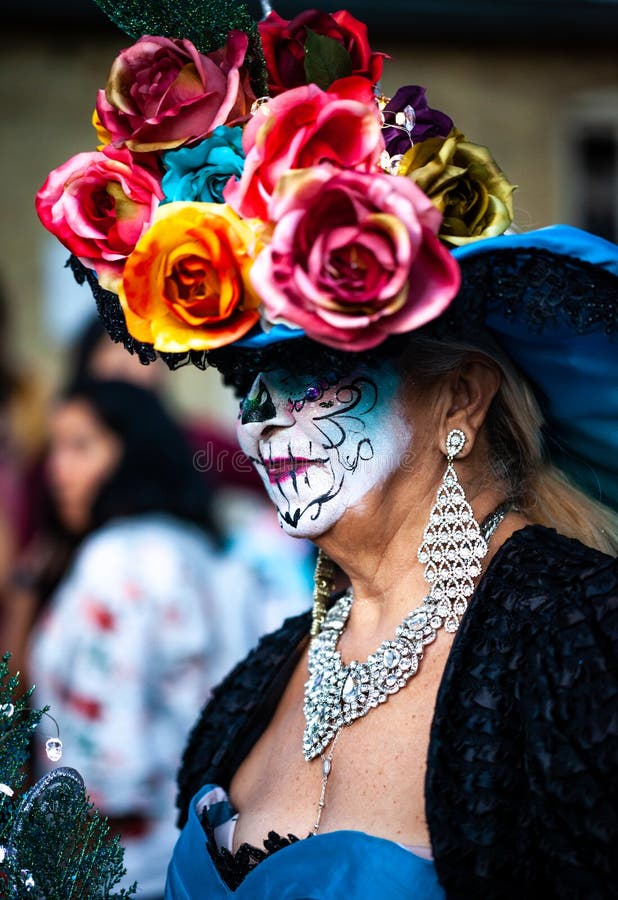 Woman with sugar skull makeup and mexican traditional paper flowers headdress attends dia de los muertos celebration.