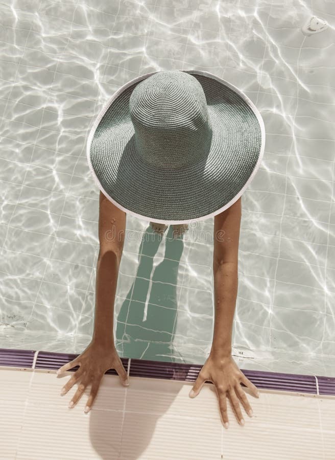 Una mujer en el sol un sombrero en nadar piscina.