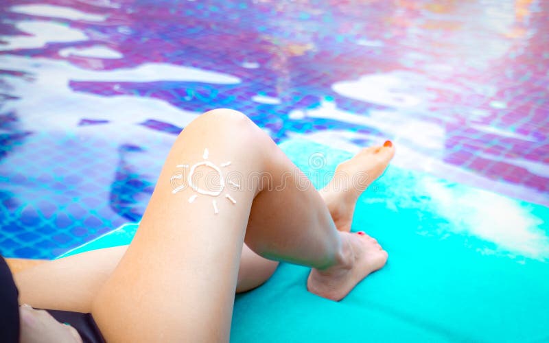 Woman with sun shape of sunscreen cream apply on tan legs. Woman sit at poolside. Woman relax on chair beside swimming pool
