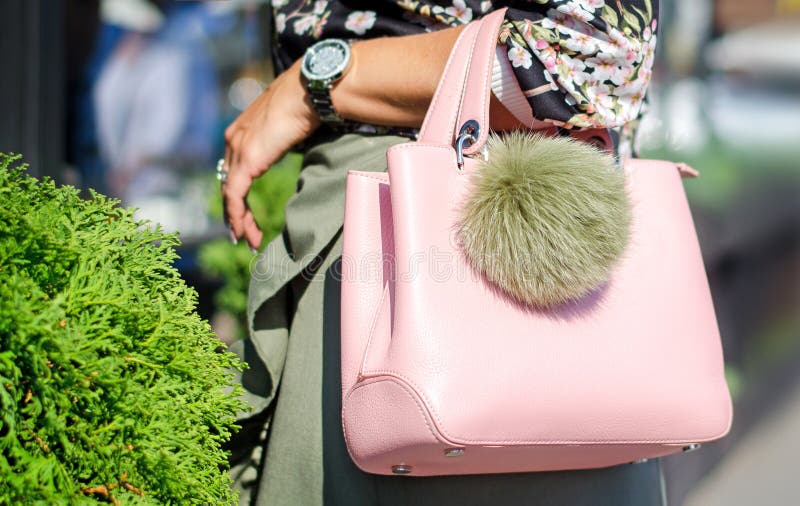 Woman on a sunny day in summer or spring with a big bag. Bag pink with keying bubo. Fashionable bag close-up in female hands.