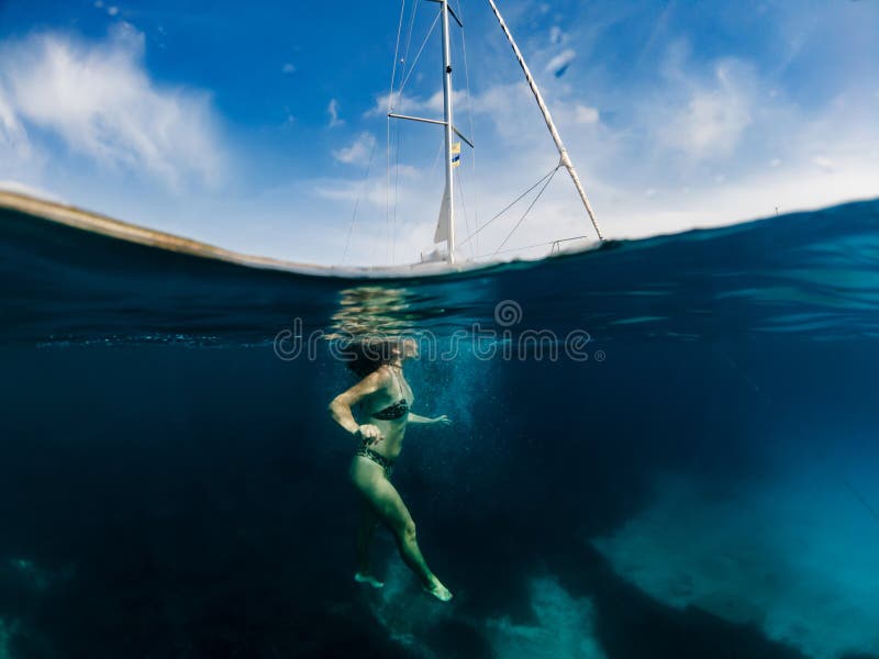 Žena je plávanie v zrušte vody z stredomoria more najbližšie jej jachta, obklopený podľa krásny prímorská krajina.