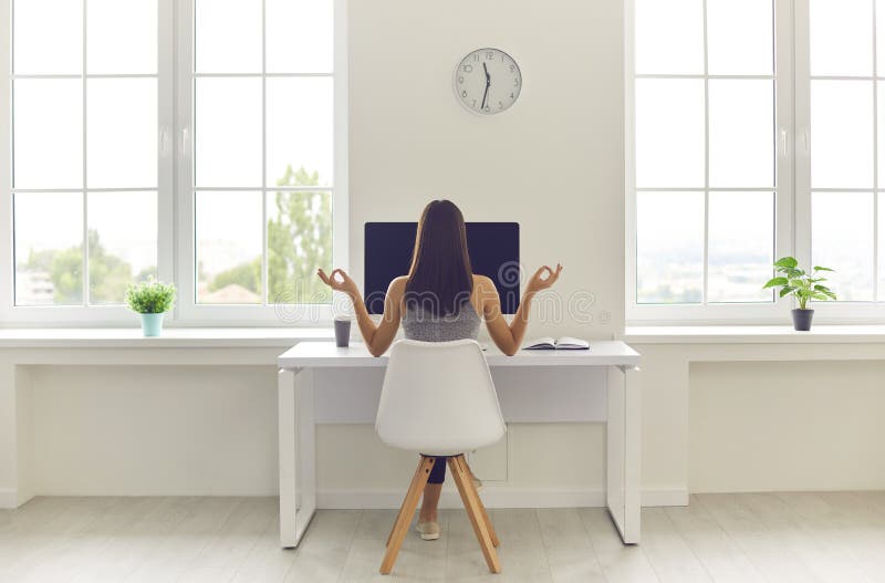 Woman taking break from work and meditating sitting at office table with computer and coffee