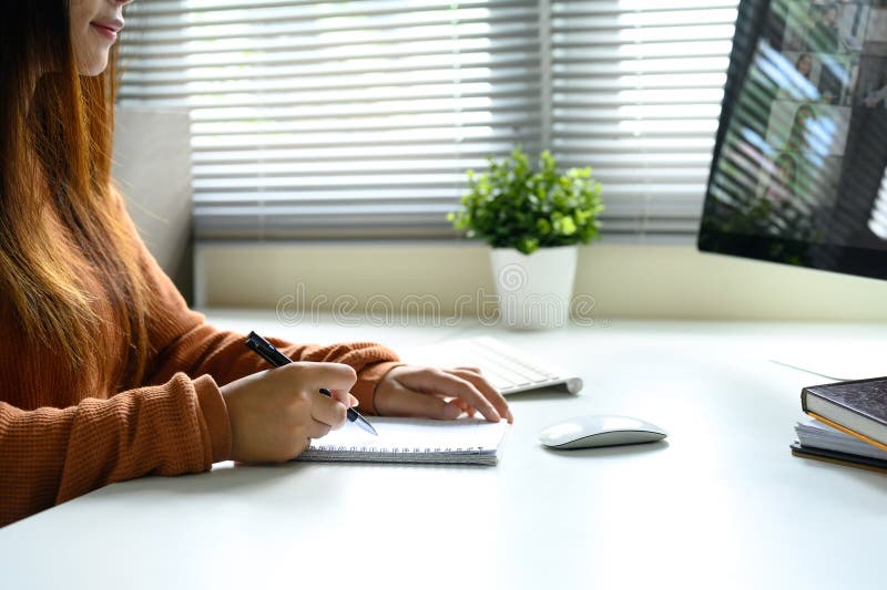 Woman taking notes during a virtual meeting while looking at a computer screen stock photo