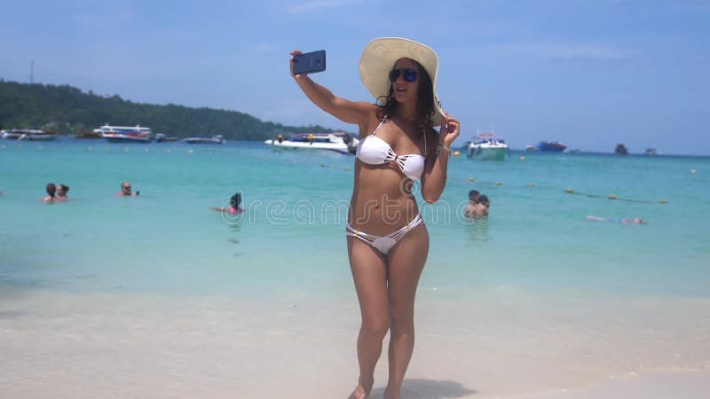 Young sexy woman in bikini taking a selfie using her mobile phone on a beautiful exotic beach in Thailand. slow motion