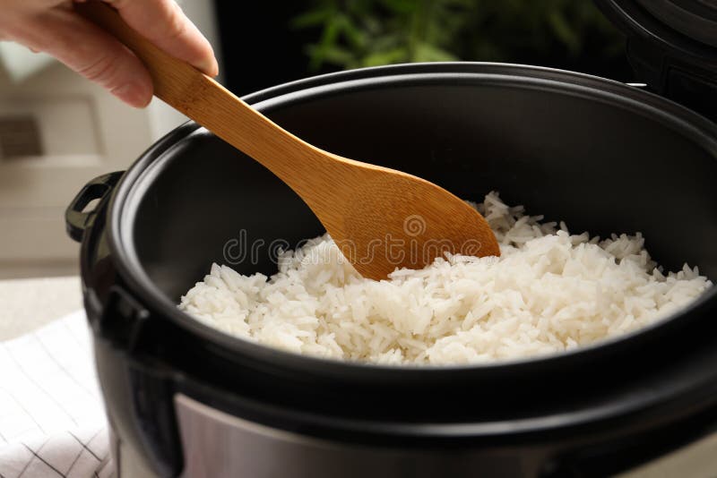 Woman taking tasty rice with spoon from cooker in kitchen stock images Woman taking tasty rice with spoon from cooker in kitchen stock images