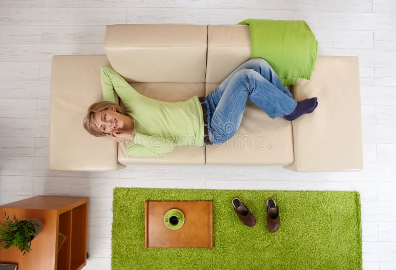 Smiling woman talking on phone,having coffee mug on tray, lying on couch, in overhead view. Smiling woman talking on phone,having coffee mug on tray, lying on couch, in overhead view.