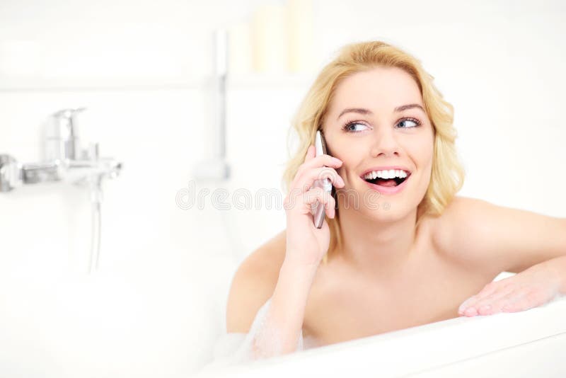 A picture of a happy woman talking on phone when taking a bath