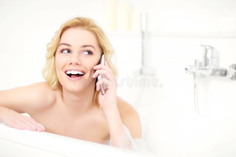 A picture of a happy woman talking on phone when taking a bath