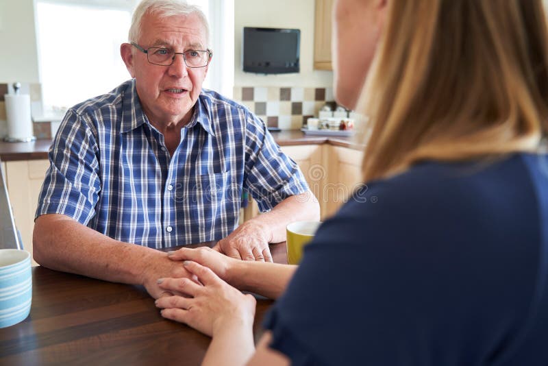 Woman Talking With Unhappy Senior Man Sitting In Kitchen At Home