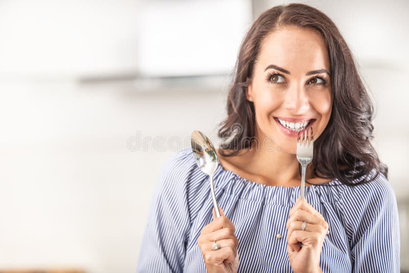 Woman thinking of eating something good bites into a fork while holding spoon in the other hand royalty free stock image
