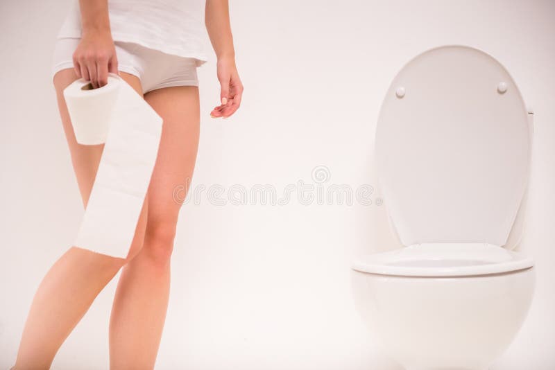 Using toilet. A young woman uses a toilet with a roll of toilet paper in his hand. Girl peeing stock images, royalty-free photos and pictures