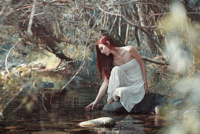 Woman touching water in a stream. Sunny woods