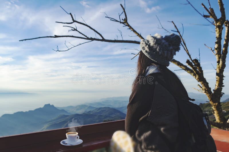 Woman traveler drinks coffee in restaurant with a view of the mountain landscape. A young tourist woman drinks a hot drink from a