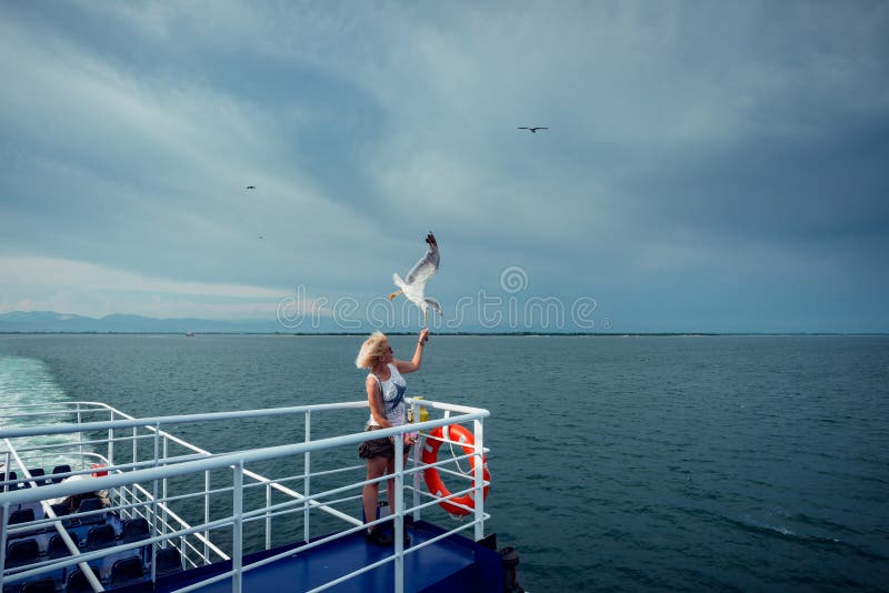 Woman traveling on ferryboat and feeding seagulls flying over the boat from deck, board