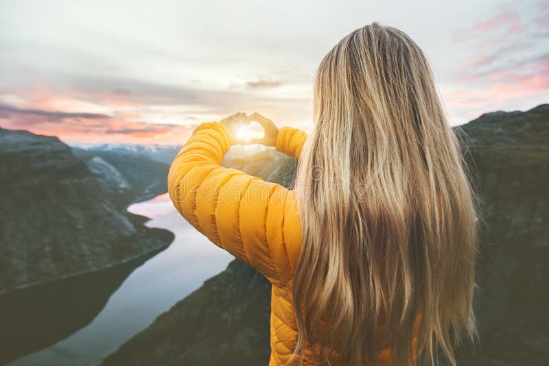 Woman traveling in sunset mountains hands heart symbol shaped