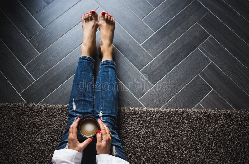 Woman in trendy blue jeans sitting on wooden grey floor, driking coffee. Top view, close up.