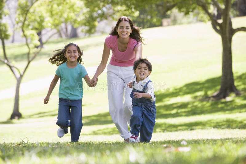 Woman with two young children running outdoors smiling. Woman with two young children running outdoors smiling