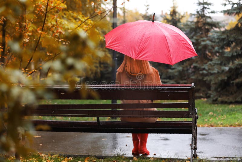 Woman with umbrella sitting on bench in autumn park